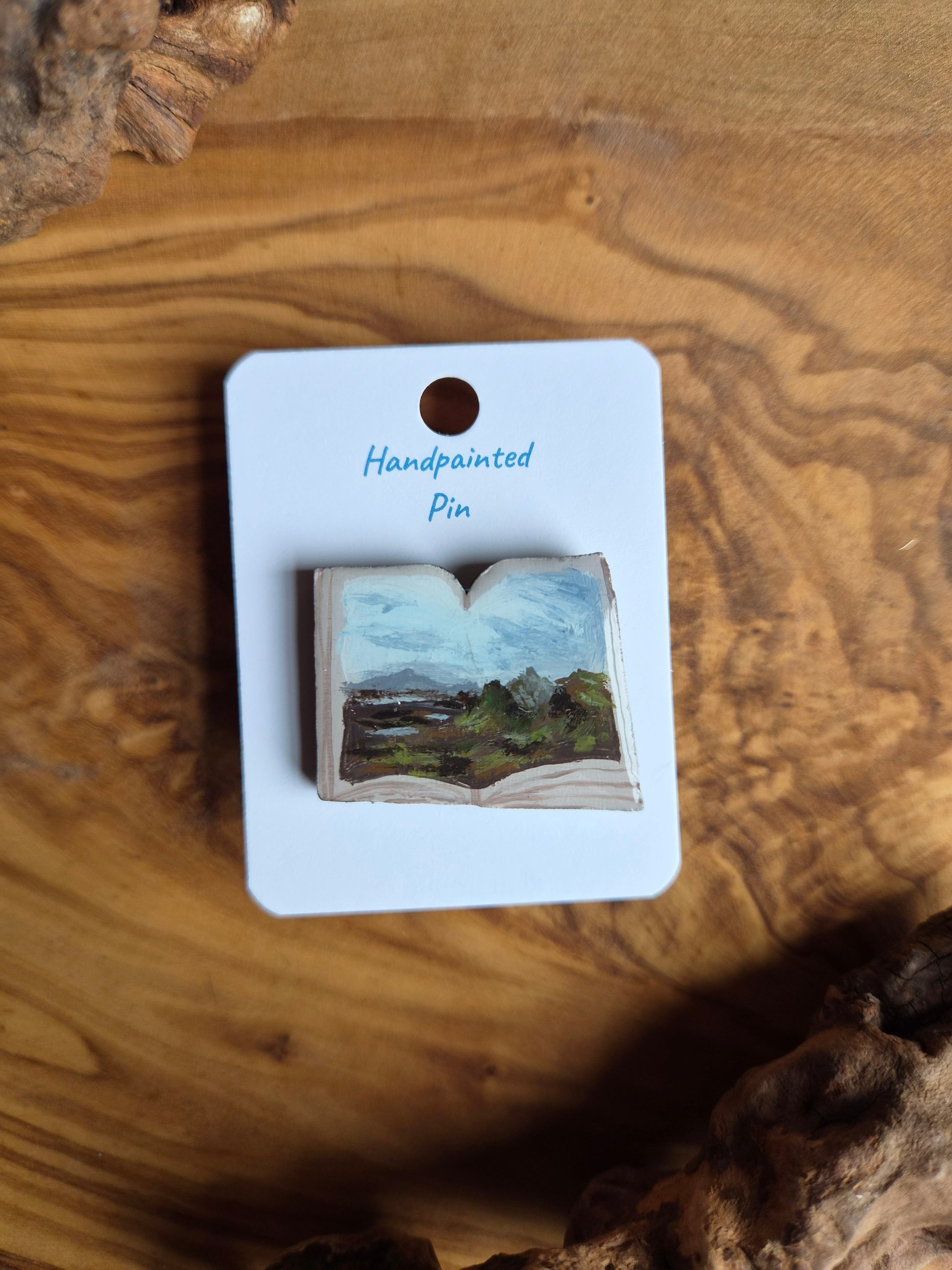 Hand-painted pin badge of an open book shape with a view of the Quiraing on the Isle of Skye, Scotland painted inside, painted onto wood
