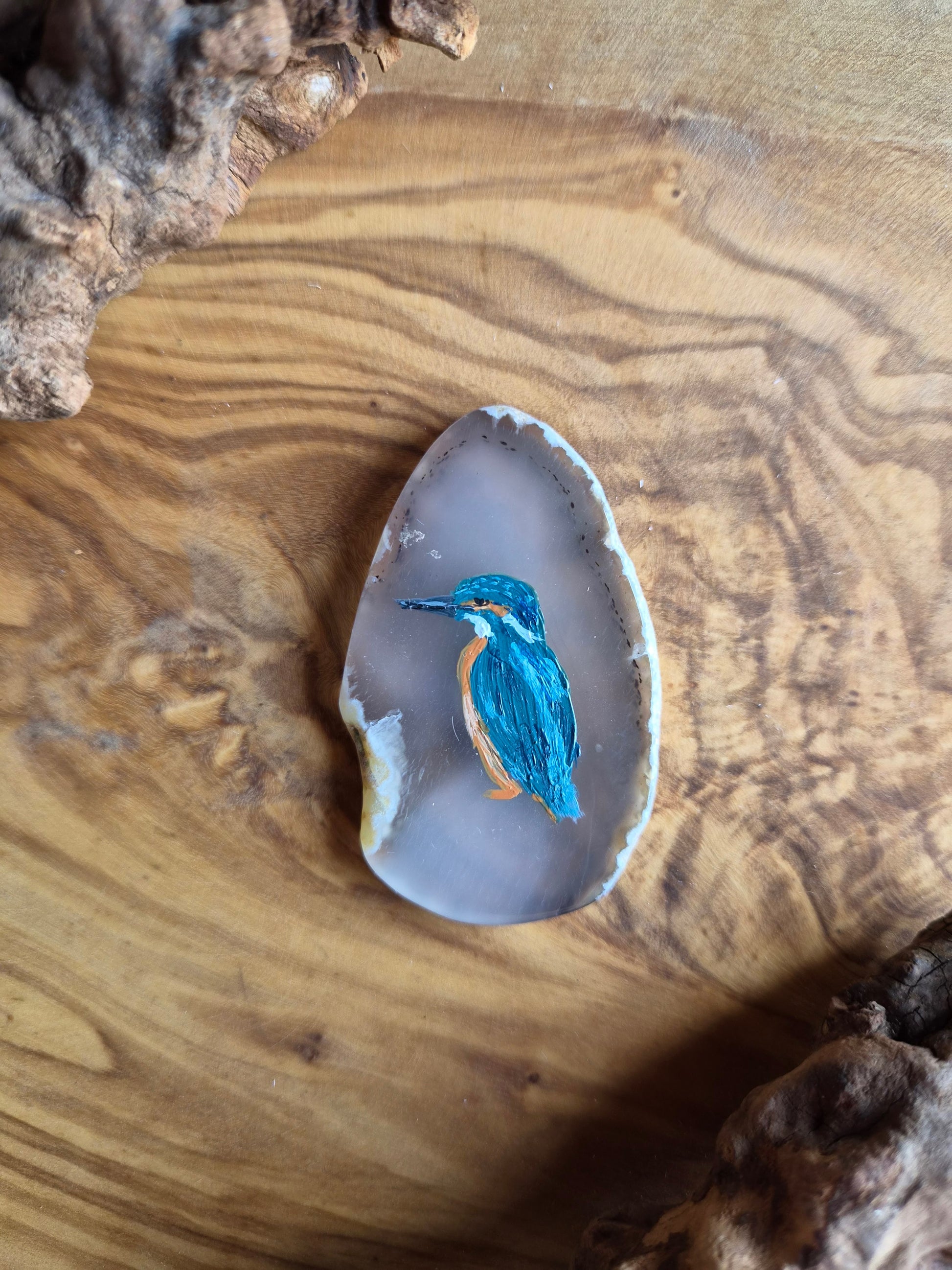 a small hand-painted natural agate slice with a painting of a kingfisher bird on it