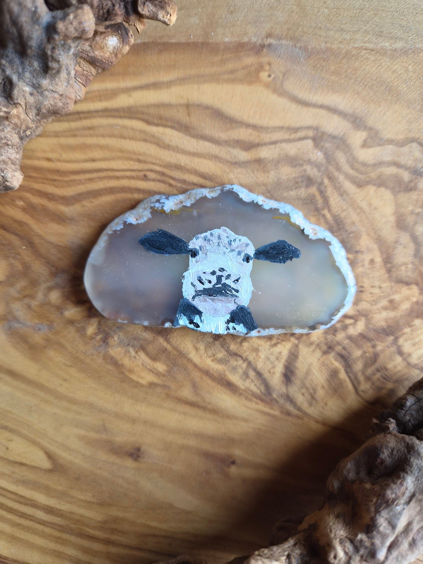 a small hand-painted natural agate slice with a painting of a cute cow face on it