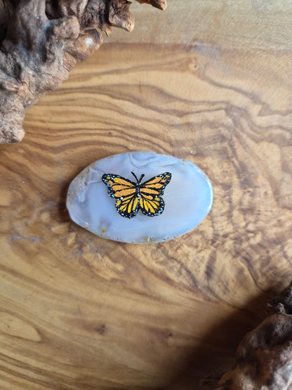 a small hand-painted natural agate slice with a painting of a butterfly on it