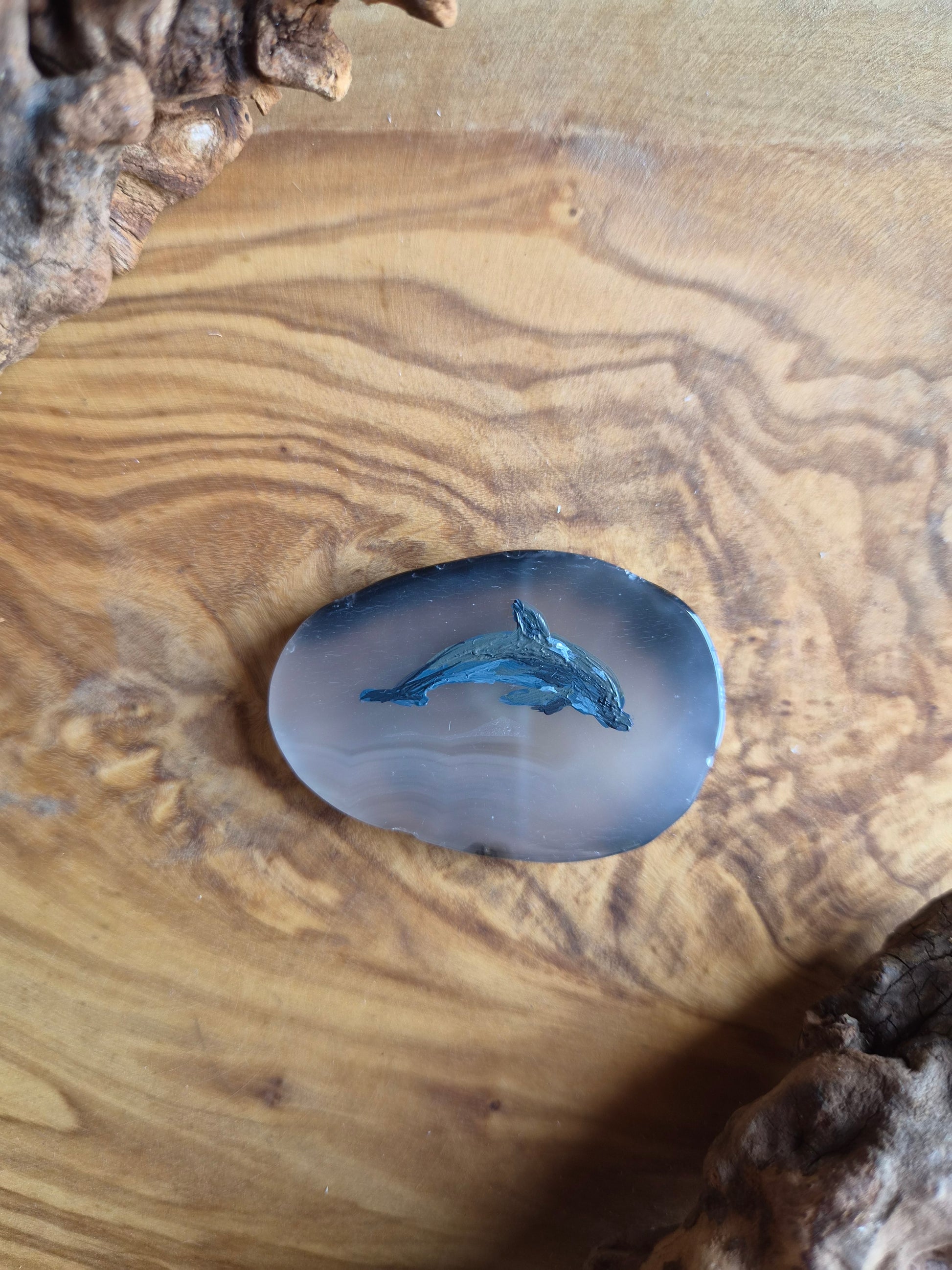a small hand-painted natural agate slice with a painting of a dolphin on it